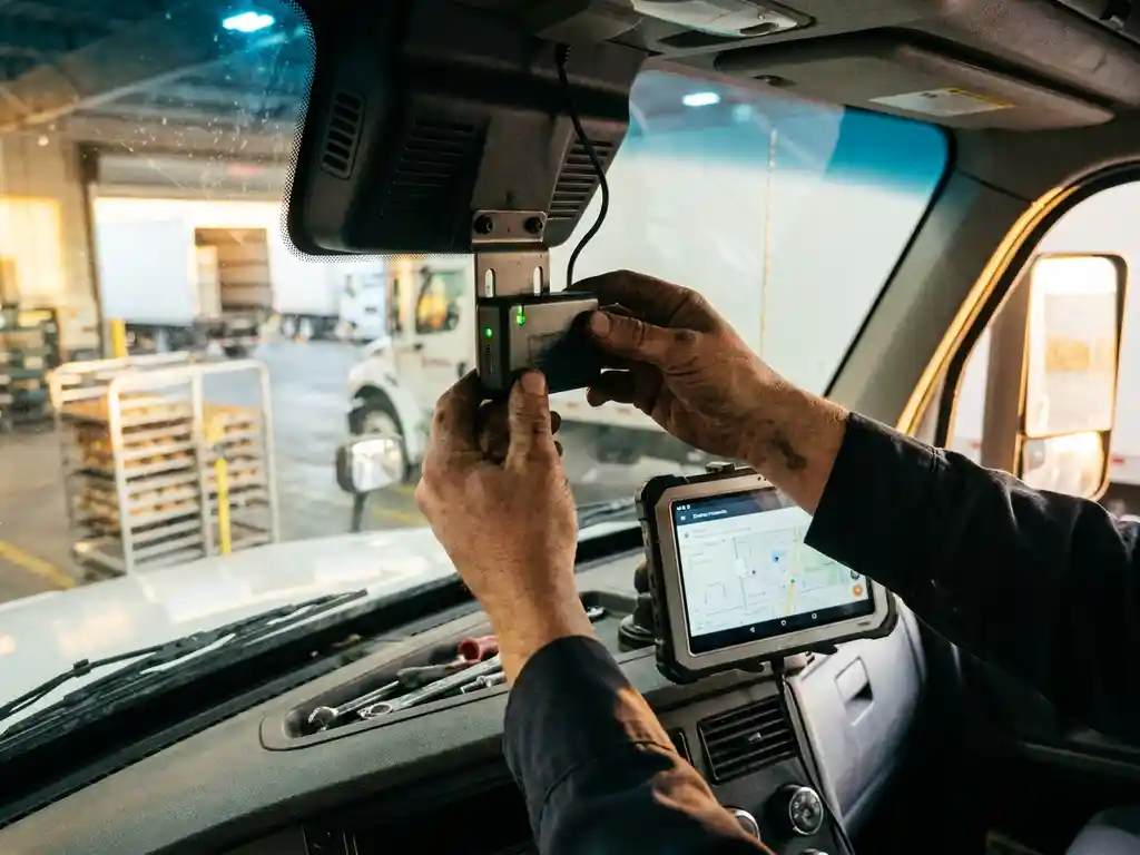 Mechaniker installiert GPS-Telematikgerät im Fahrerhaus eines Lieferwagens, Armaturenbrett mit Tablet im Hintergrund sichtbar.