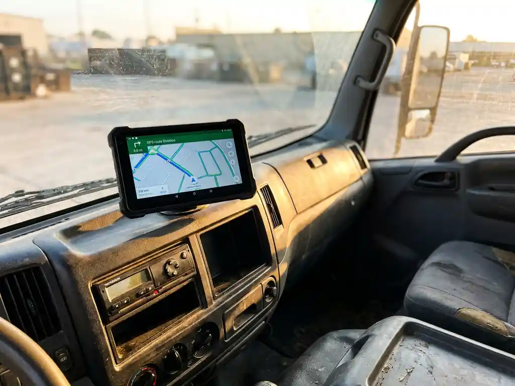 Lkw-Fahrerhaus mit Tablet-Routennavigation und digitalem Tachographen im Armaturenbrett, warmes Morgenlicht durch die Windschutzscheibe.